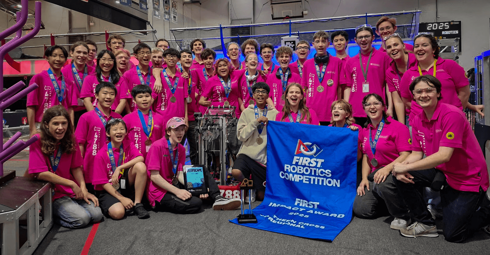 Team 4788 in pink shirts with their robot and a FIRST Robotics Competition banner