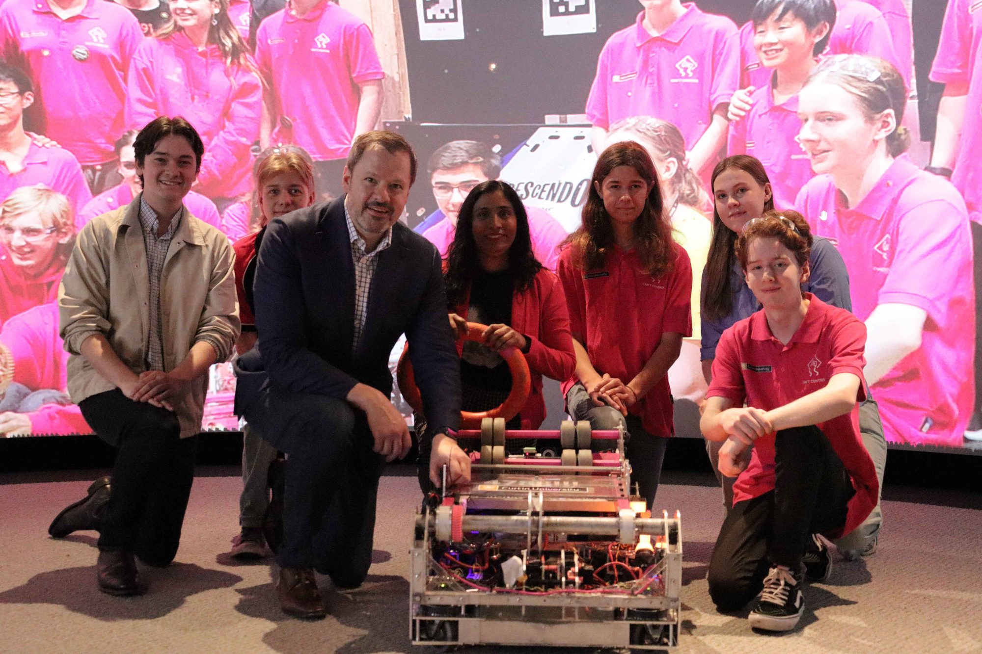 Team members and guests kneeling beside the robot on stage